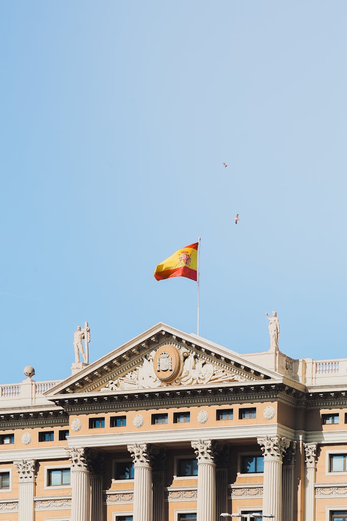 A classic building facade in Barcelona displaying the Spanish flag under a clear blue sky.