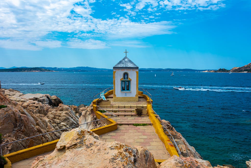 A picturesque chapel atop rocky cliffs, overlooking the vibrant blue sea in Porto Cervo, Sardinia.