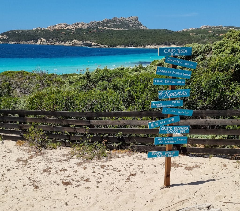 Beautiful Sardinian beach with a directional signpost pointing to global landmarks.