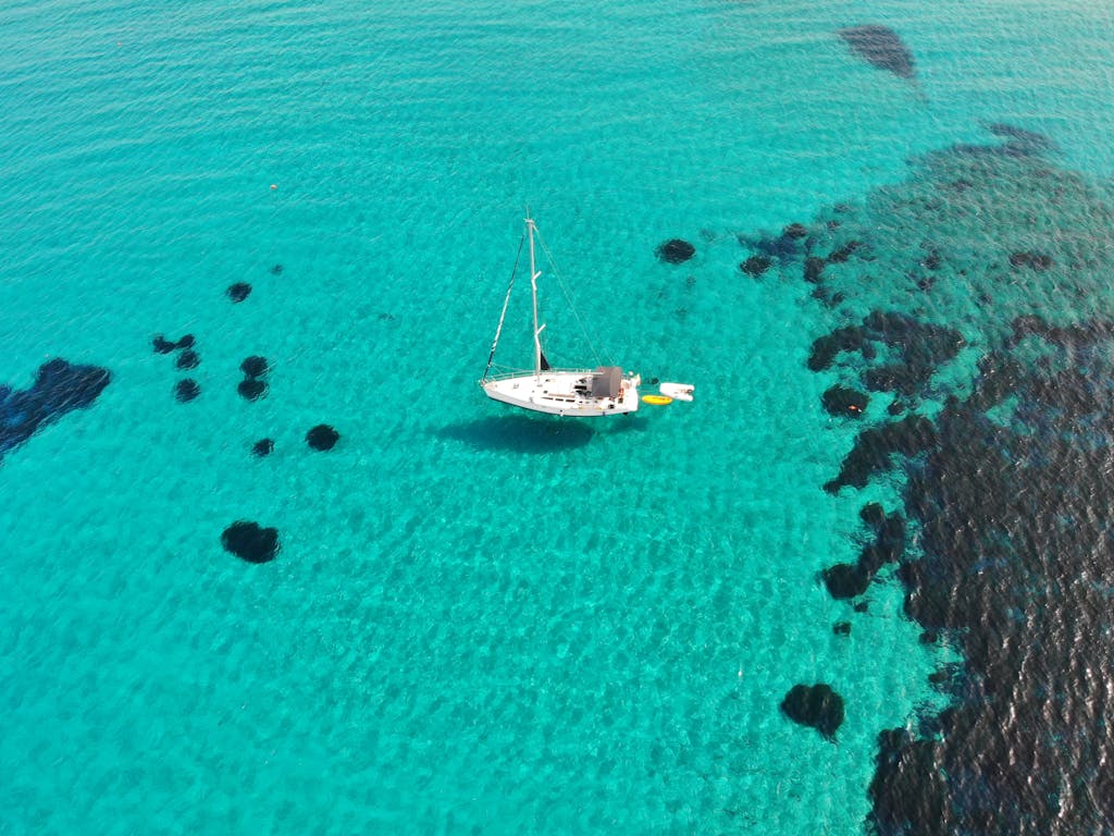 Captivating aerial shot of a sailboat in the turquoise waters near Geremeas, Sardegna, Italy.